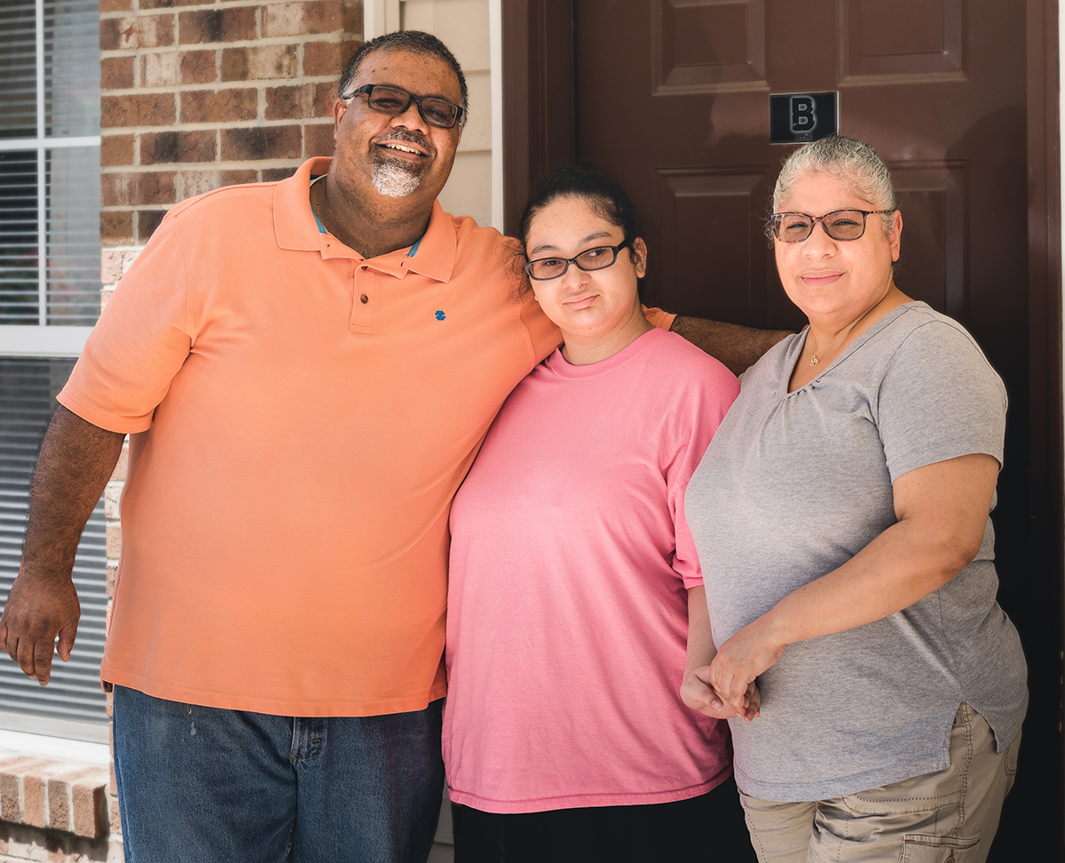 A family of three smiling together in front of their CASA home